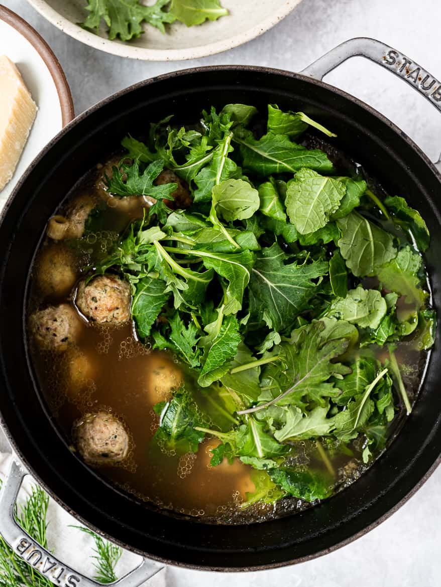 Adding leafy greens to Italian wedding soup pot.