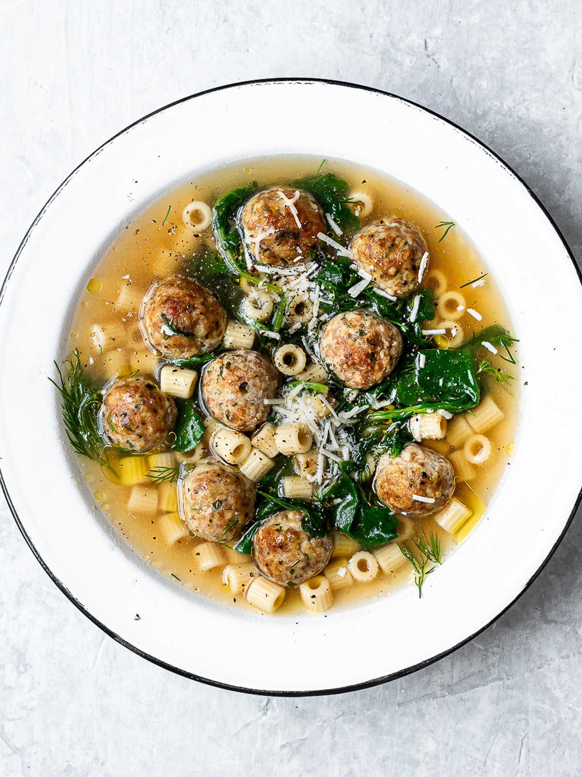 Italian wedding soup served in a white bowl garnished with parmesan cheese.