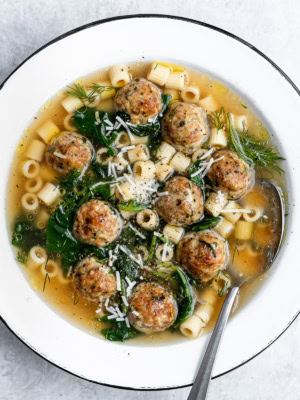 closeup of Italian wedding soup served in a white bowl garnished with parmesan cheese