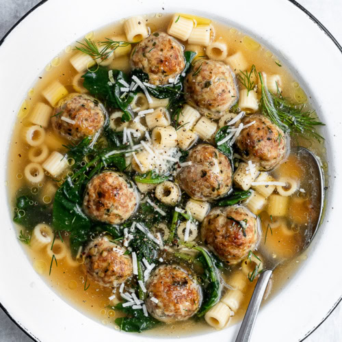 closeup of Italian wedding soup served in a white bowl garnished with parmesan cheese