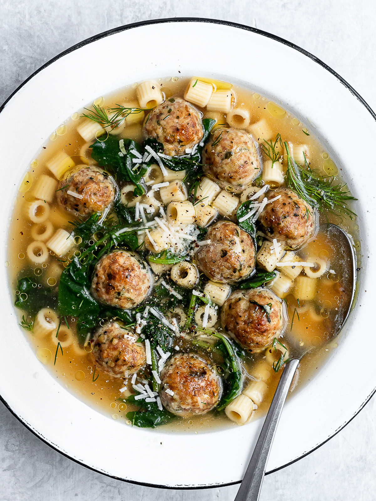 Closeup of Italian wedding soup served in a white bowl garnished with parmesan cheese.