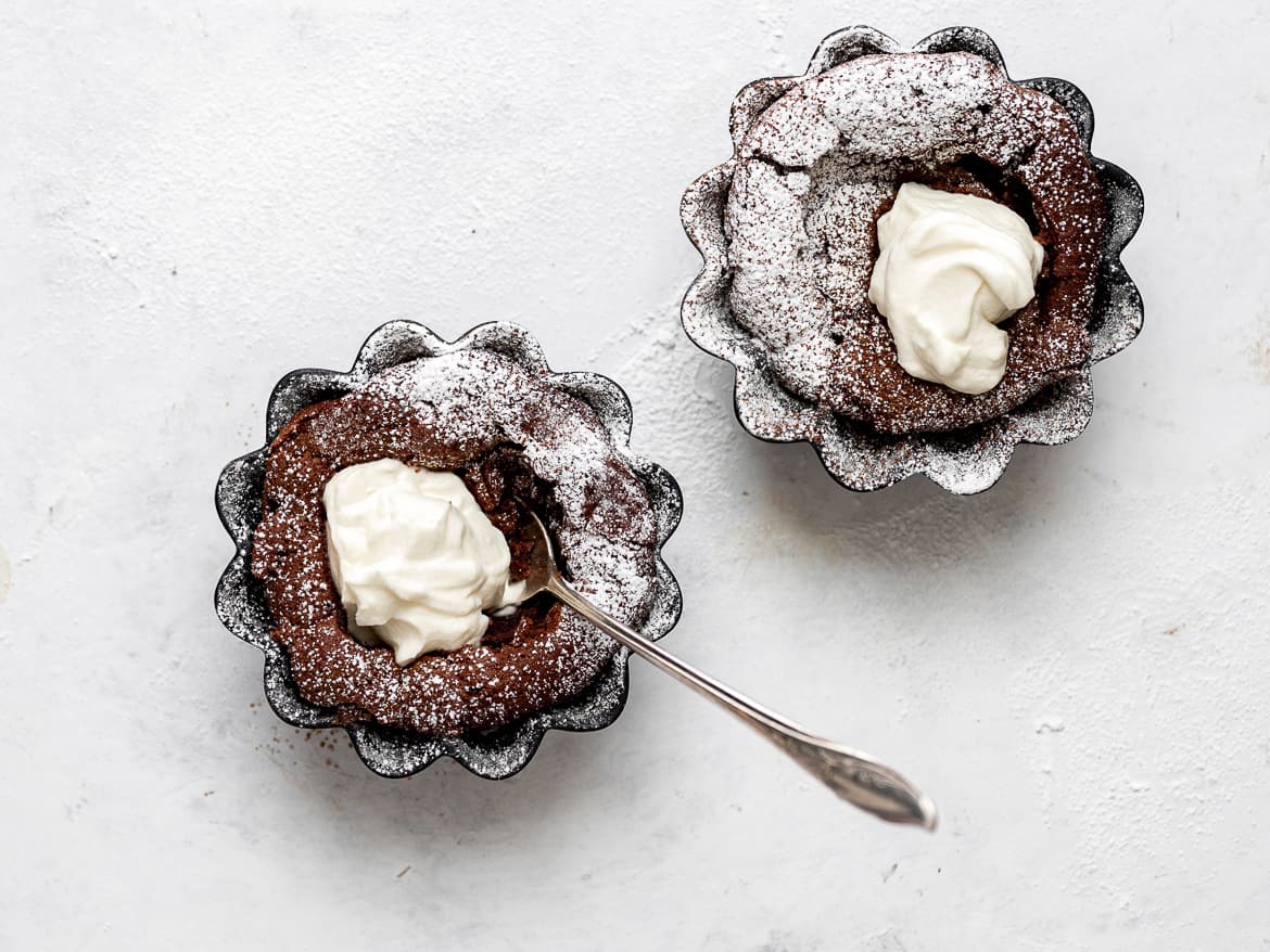 2 baked Fallen Chocolate Soufflé Cakes with whipped mascarpone cream and dusting of powdered sugar