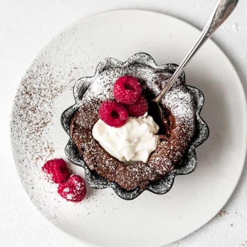 Individual Fallen Chocolate Soufflé Cakes with whipped mascarpone cream and dusting of powdered sugar and fresh raspberries