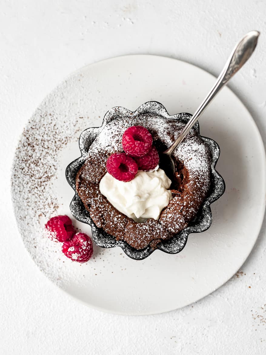 Individual Fallen Chocolate Soufflé Cakes with whipped mascarpone cream and dusting of powdered sugar and fresh raspberries