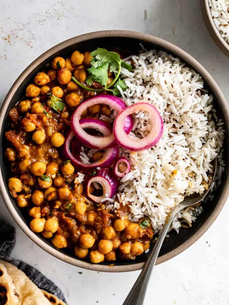 close up of Chana Masala served in bowl with rice and topped with pickled onions