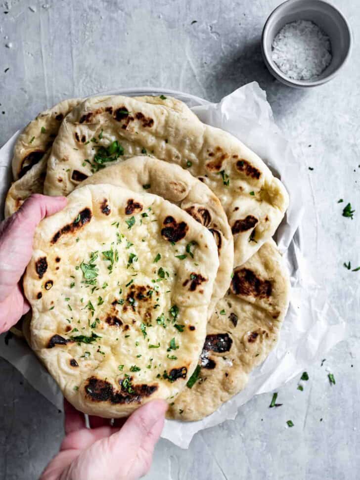 hands picking up a slice of Homemade Naan with butter and flaky salt