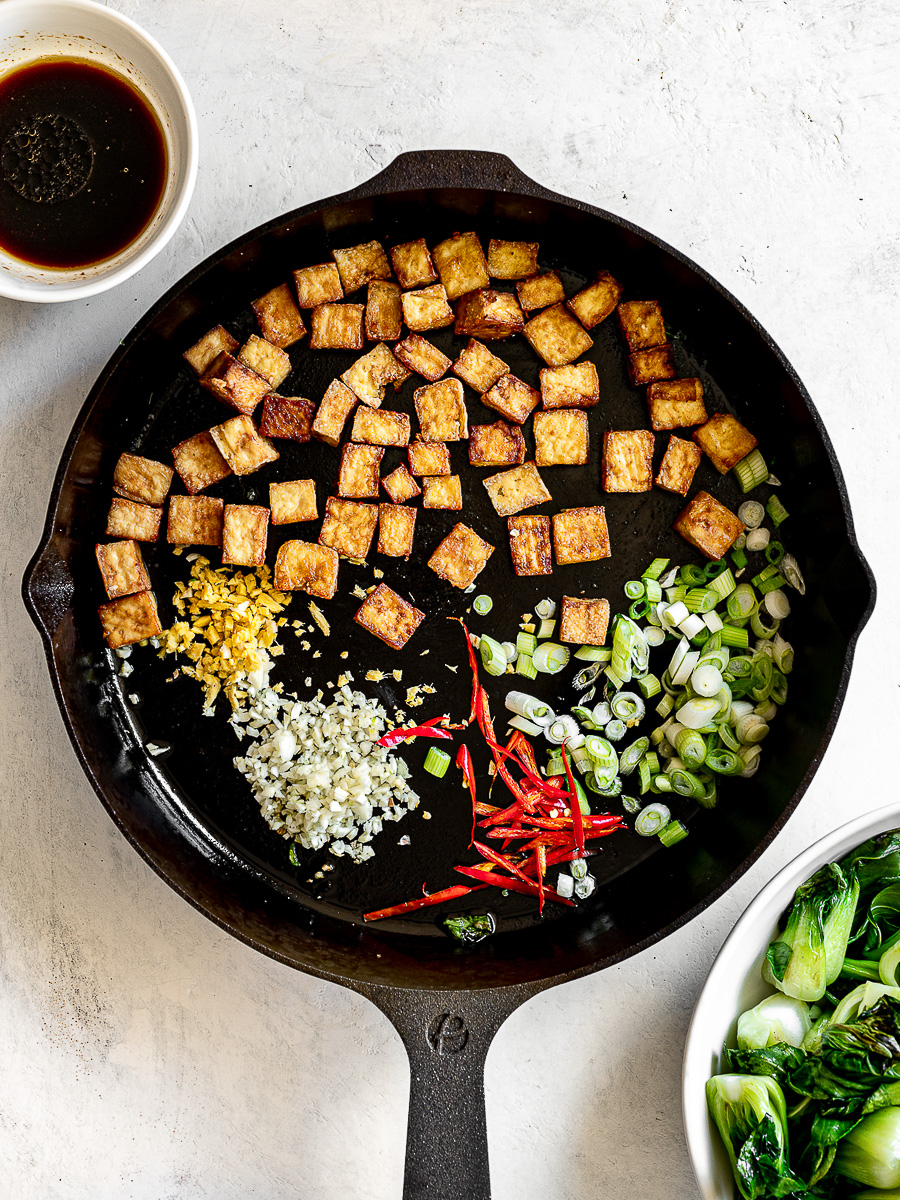 Stir frying tofu cubes with ginger, garlic, stir-fry sauce and scallions in skillet. 