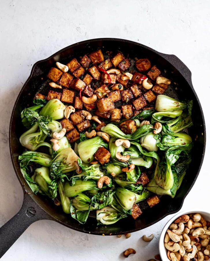 Tofu and Bok Choy stir fry in skillet with cashews in bowl