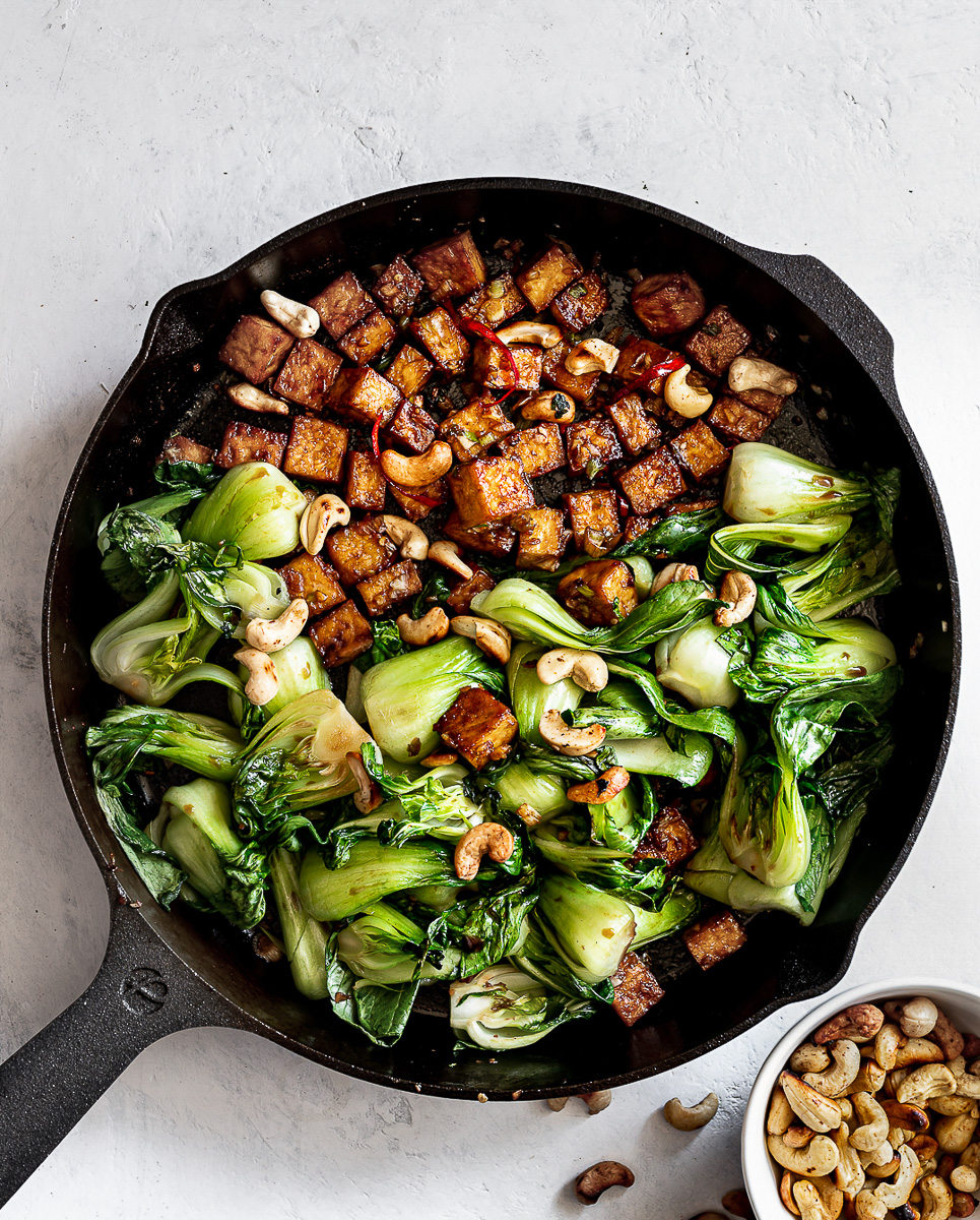 Tofu and Bok Choy stir-fry tossed together in skillet with toasted cashews on the side. 