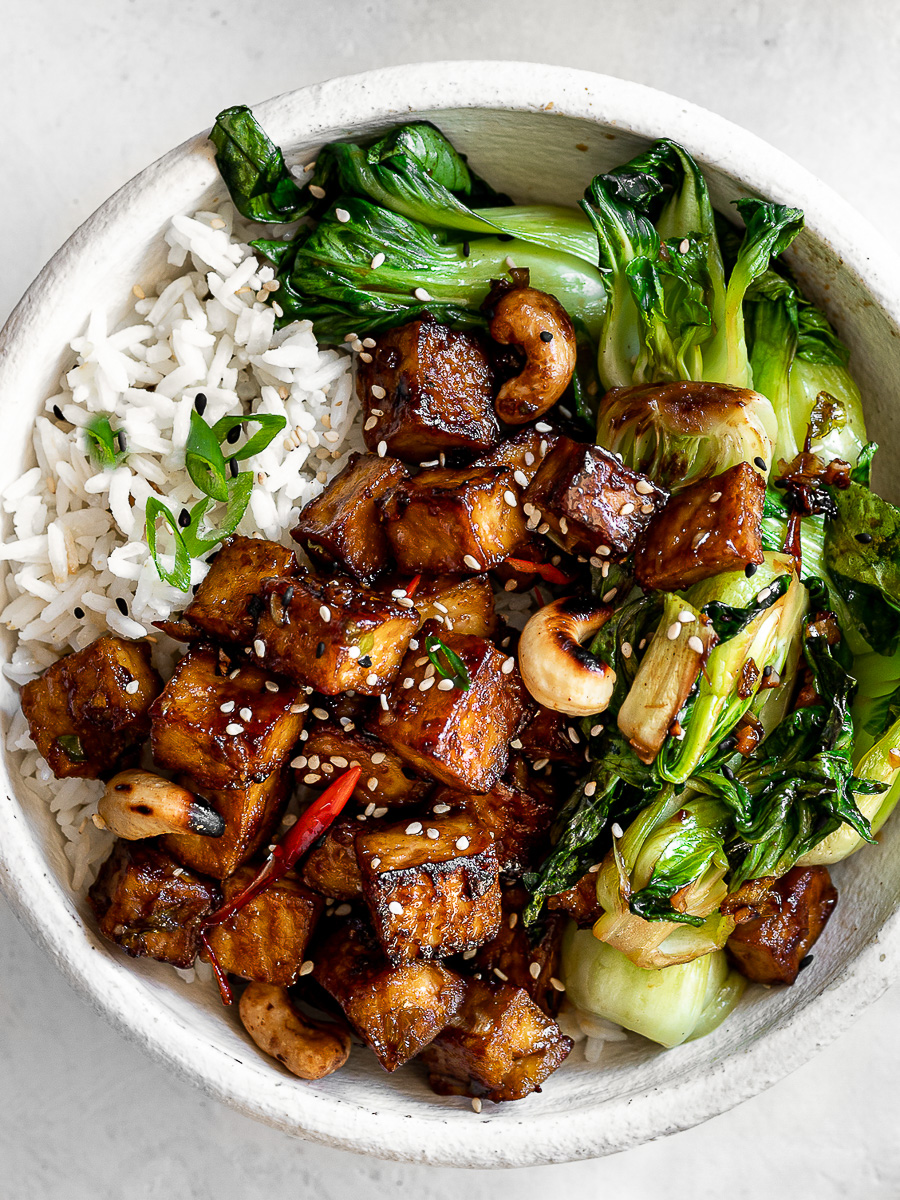 Close-up of tofu and Bok Choy stir fry served in white bowl over rice.