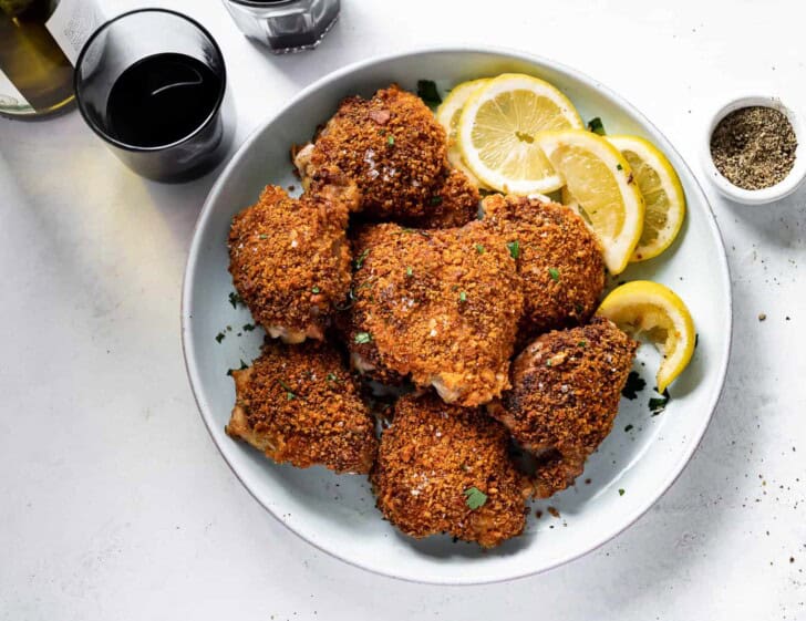 crispy baked chicken thighs on plate with glass of wine 