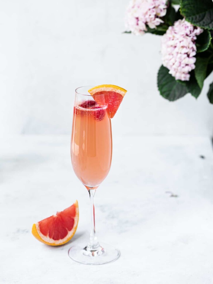 One single Grapefruit mimosa with raspberries in tall champagne flute