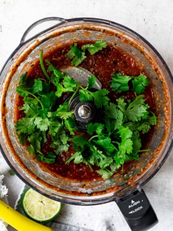 adding cilantro to blended salsa in food processor