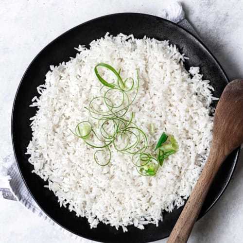 Coconut rice garnished with scallions in serving bowl