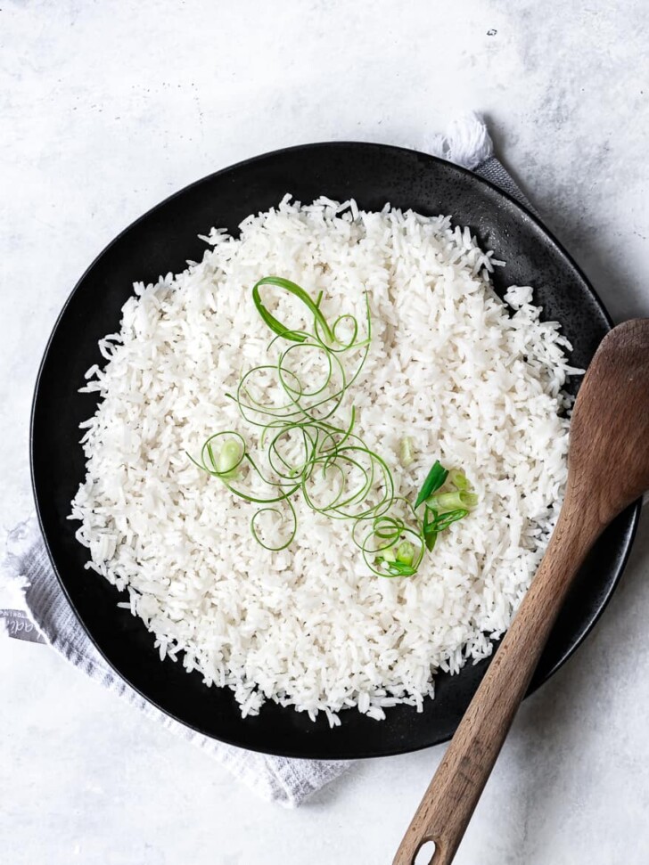 Coconut rice garnished with scallions in serving bowl