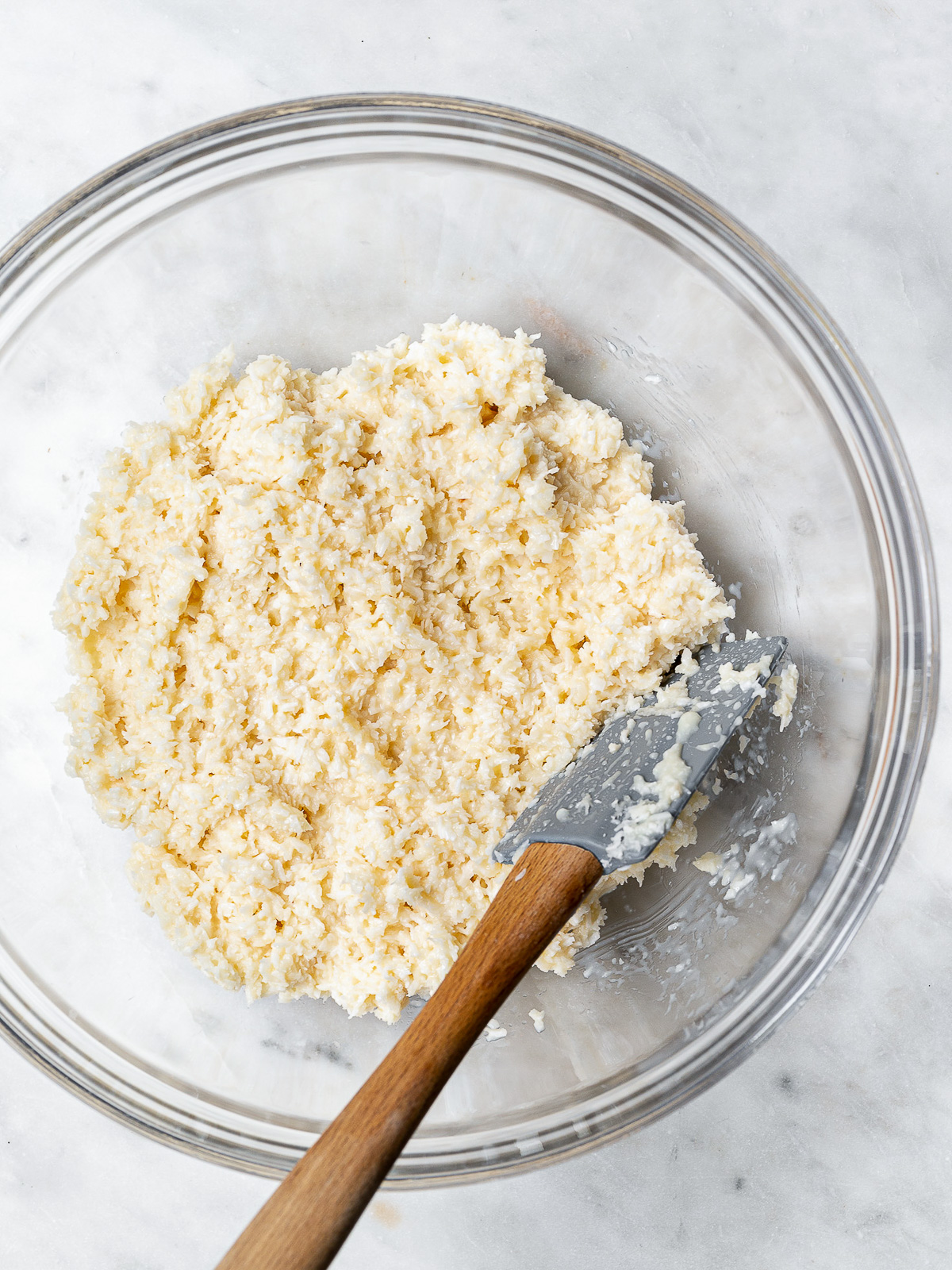 Shredded coconut mixed with sweetened condensed milk in mixing bowl.