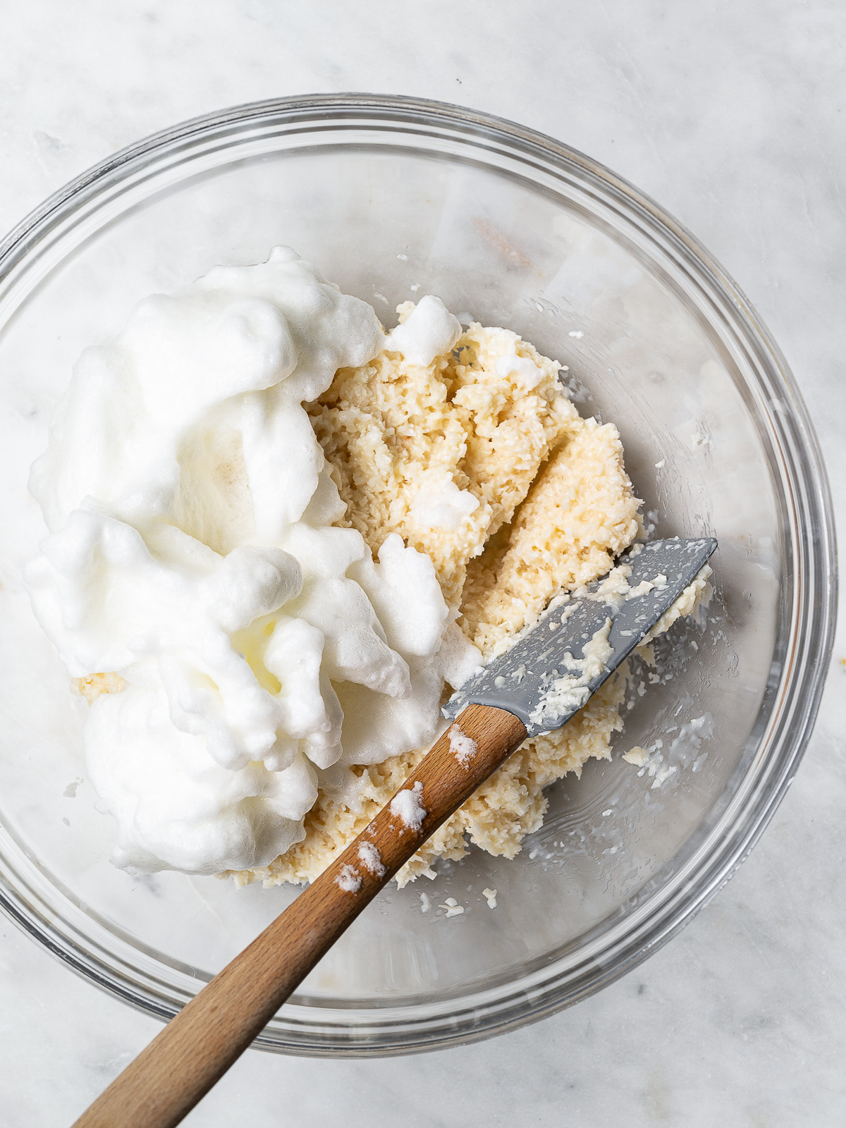 Adding egg whites to Shredded coconut mixed with sweetened condensed milk in mixing bowl.