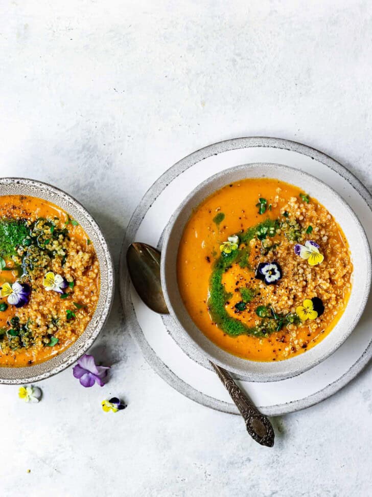 Creamy zucchini and tomato soup in bowl topped with quinoa and basil oil