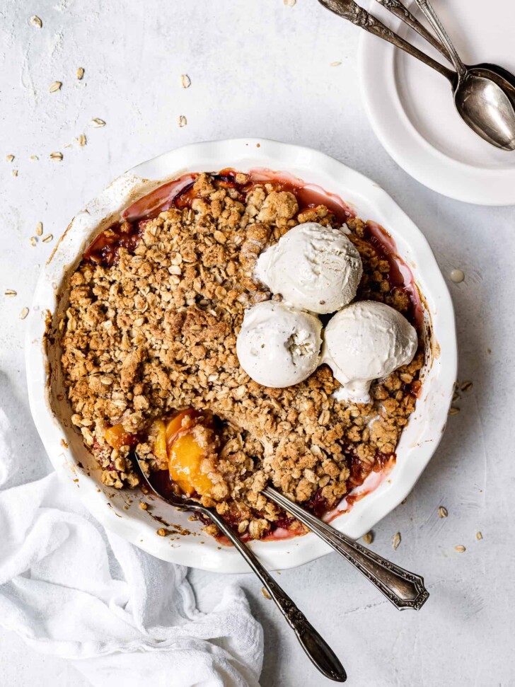 baked Peach crisp in pie dish with ice cream scoops on top