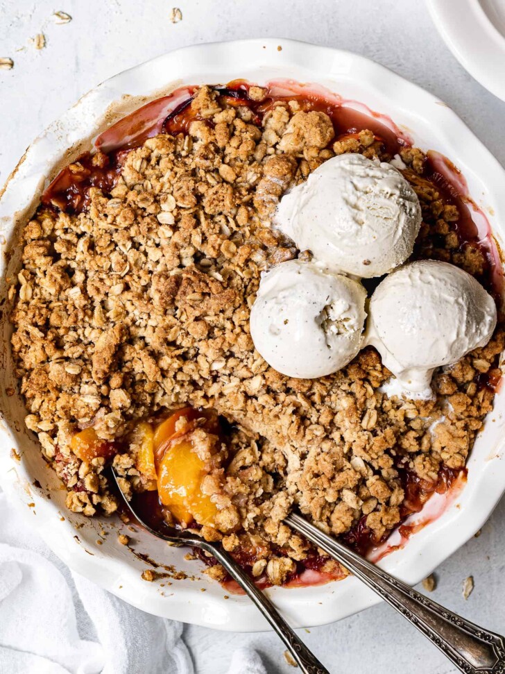 close-up of baked Peach crisp in pie dish with ice cream scoops on top