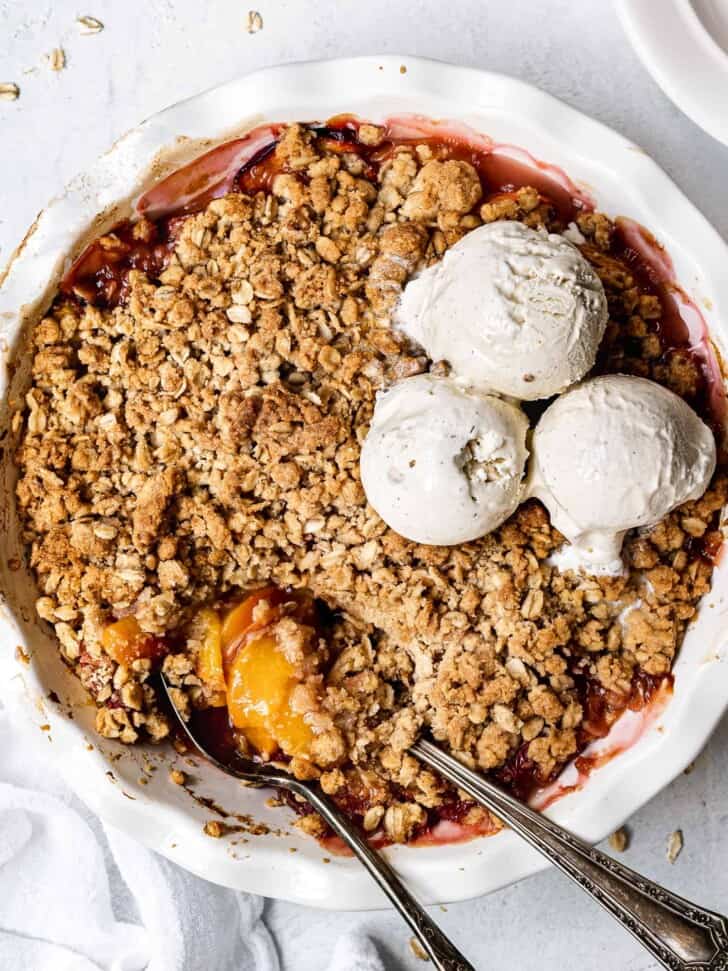 close-up of baked Peach crisp in pie dish with ice cream scoops on top