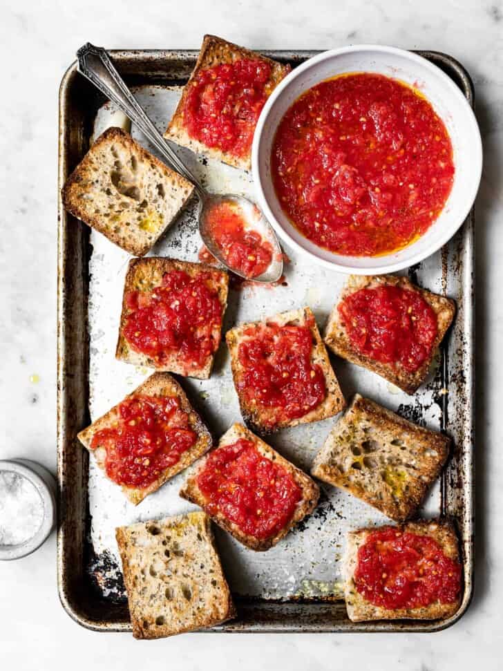 Toasted bread getting topped with tomato pulp 