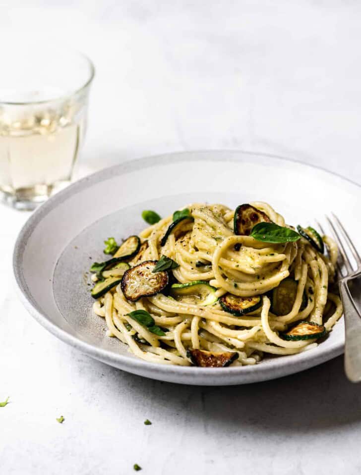 side view of spaghetti alla Nerano served in a bowl with glass of wine