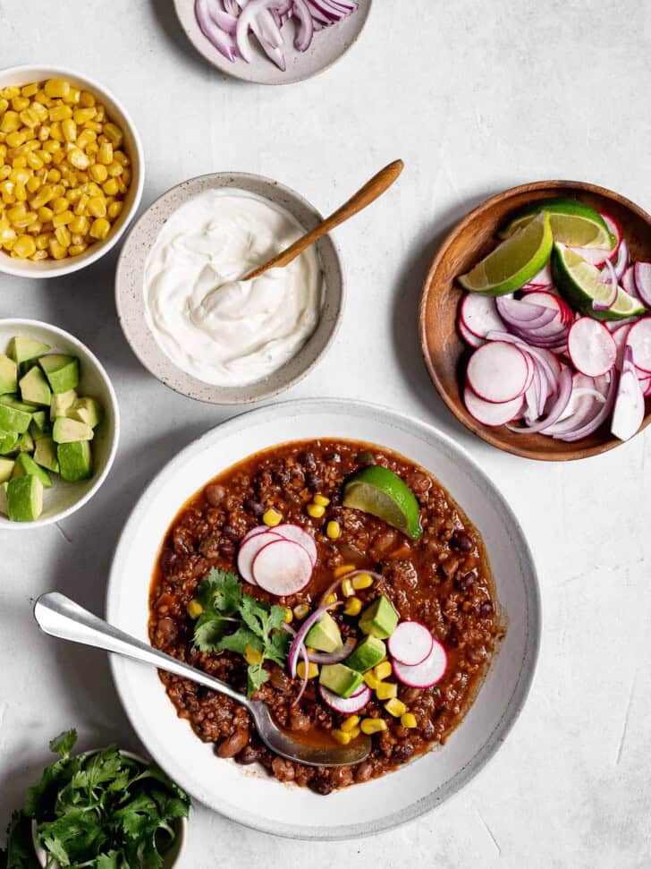 Vegan chili in bowl with toppings on the side in bowls