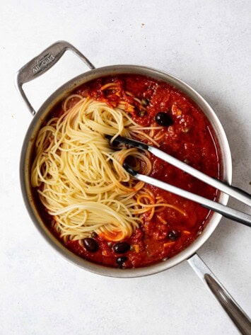 spaghetti noodles added to sauce in saucepan