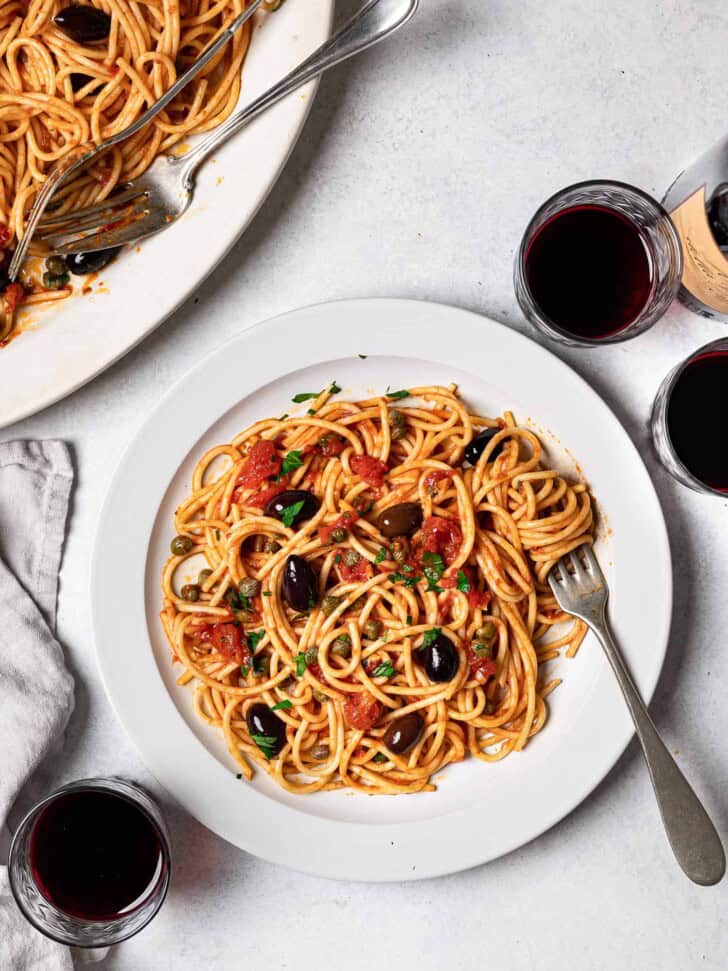 pasta puttanesca served on plate with wine glasses