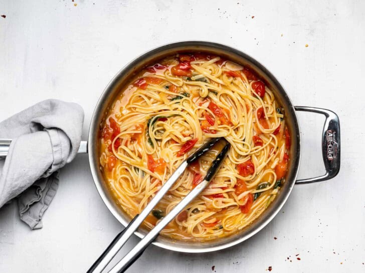 stirring pasta in pan with tongs