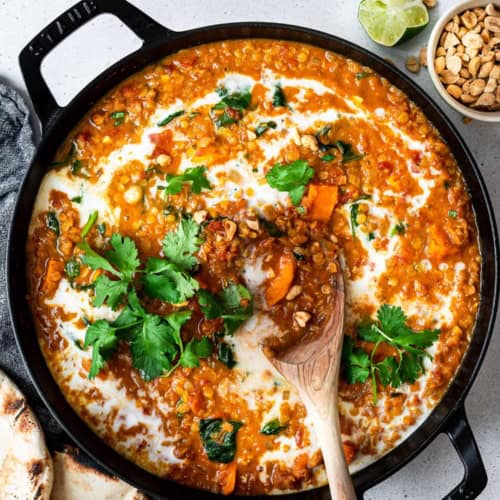 curried red lentil soup in pan shown with flat bread and peanuts on the side
