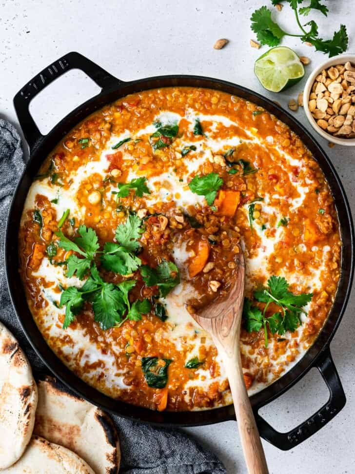 curried red lentil soup in pan shown with flat bread and peanuts on the side