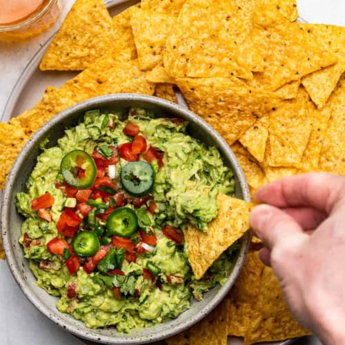 The best guacamole served in a bowl with a hand dipping a tortilla chip