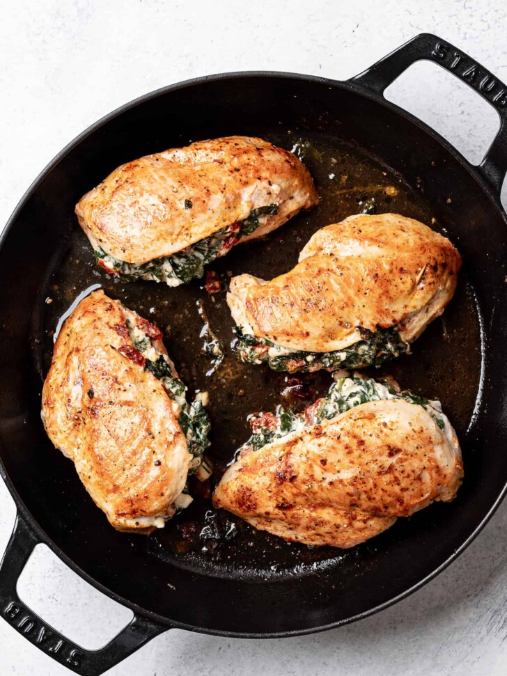 close up of cooked spinach and feta stuffed chicken breasts in skillet 