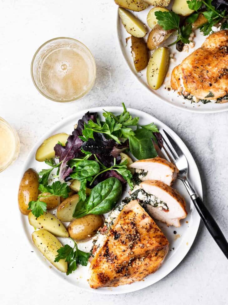 Spinach and feta stuffed chicken served on two plates with potatoes and salad