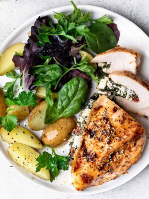 Spinach and feta stuffed chicken served on plate with potatoes and salad