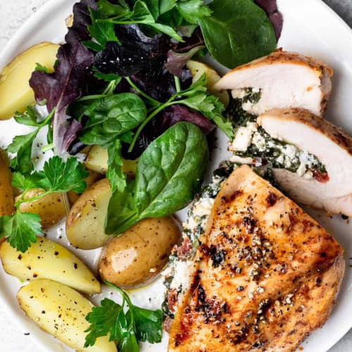 Spinach and feta stuffed chicken served on plate with potatoes and salad