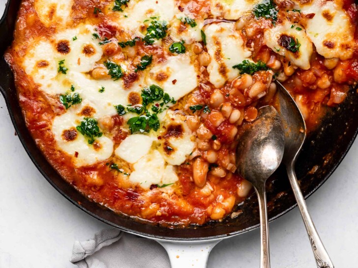 close up of cheesy baked beans with tomatoes drizzled with parsley oil