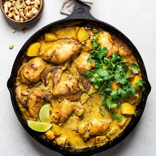 Thai yellow chicken curry in skillet garnished with cilantro and lime wedges