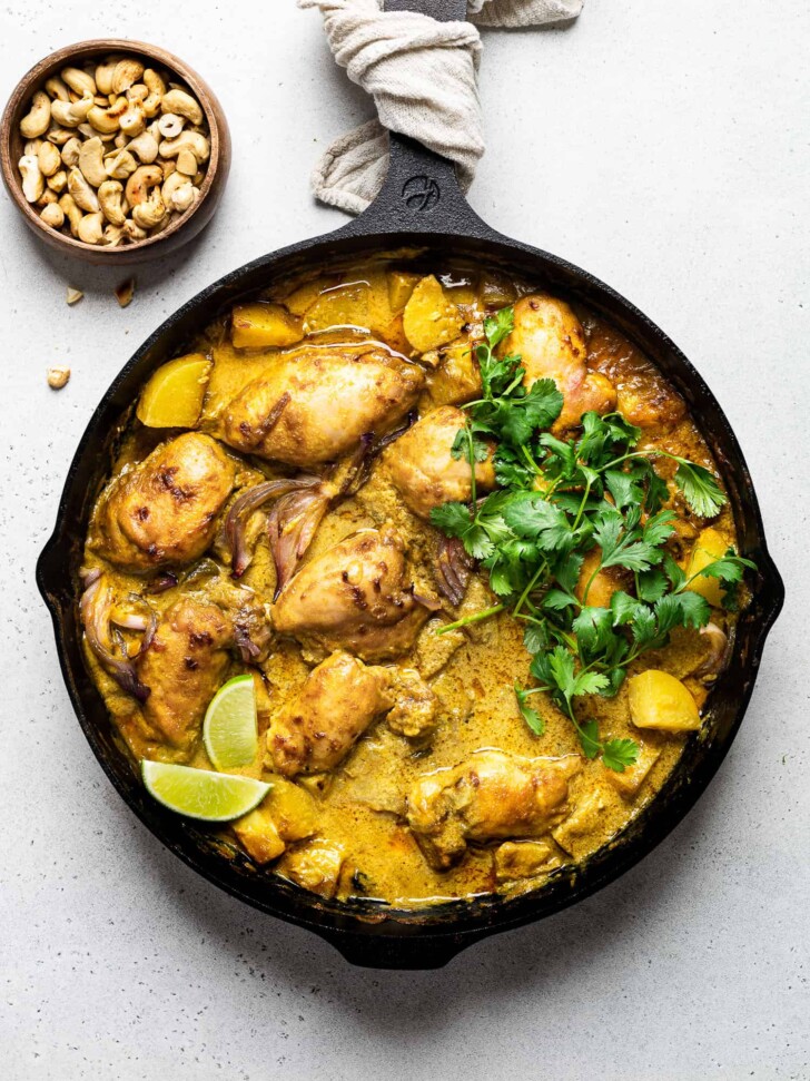 Thai yellow chicken curry in skillet garnished with cilantro and lime wedges 