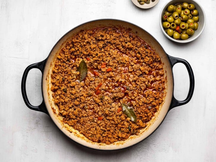 Cooked ground turkey mixture in saucepan with a small bowl of green olives on the side. 