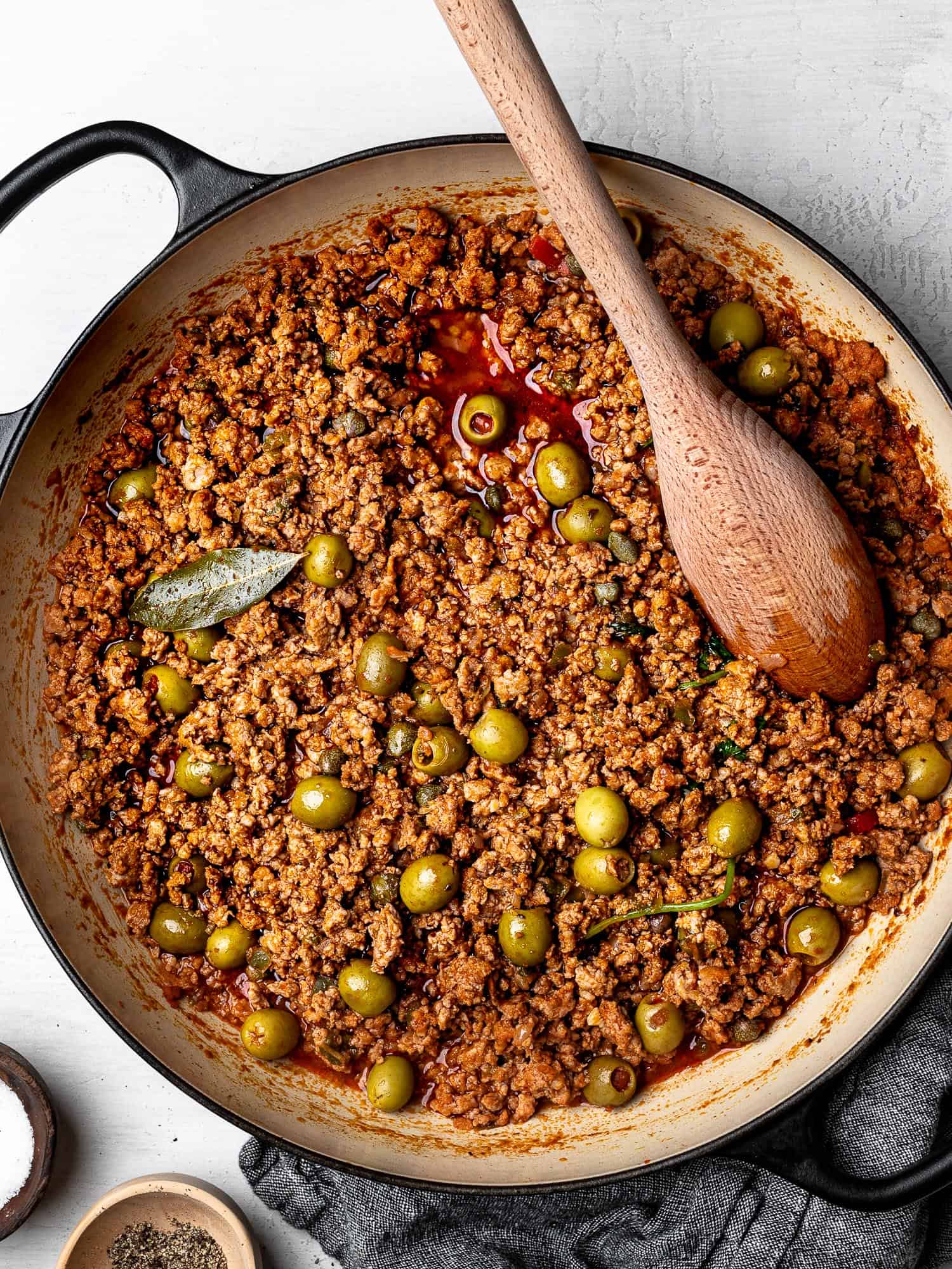 Finished dish of turkey picadillo with olives in saucepan and a wooden spoon for serving.