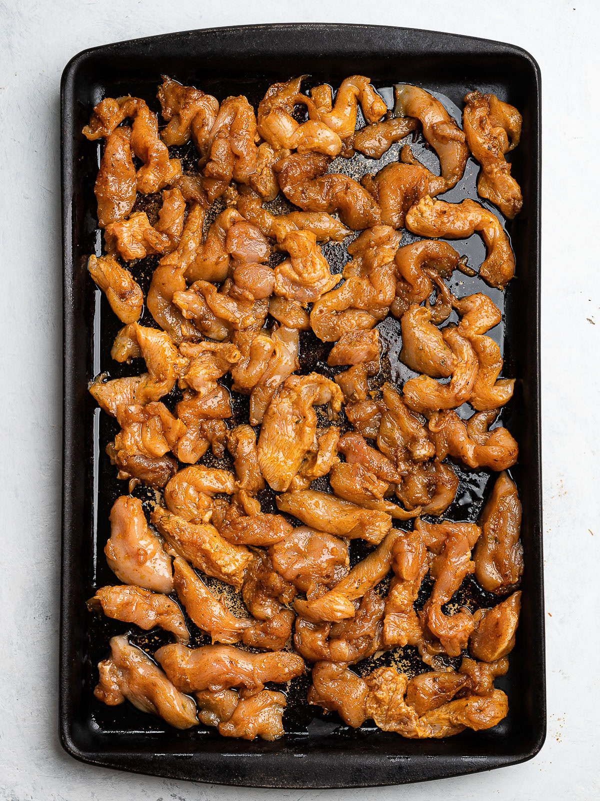 marinated chicken pieces spread out on baking sheet