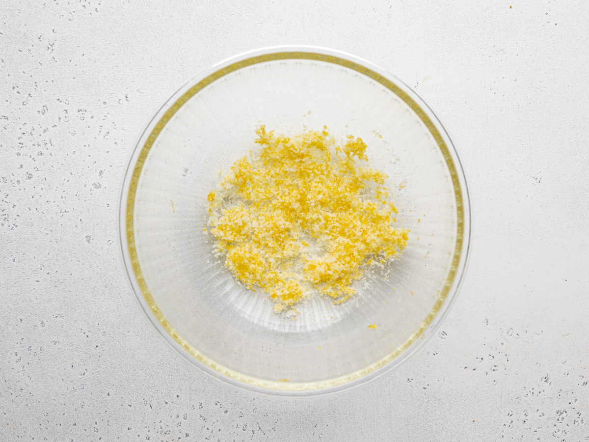 Lemon zest and sugar mixed in a large glass mixing bowl.