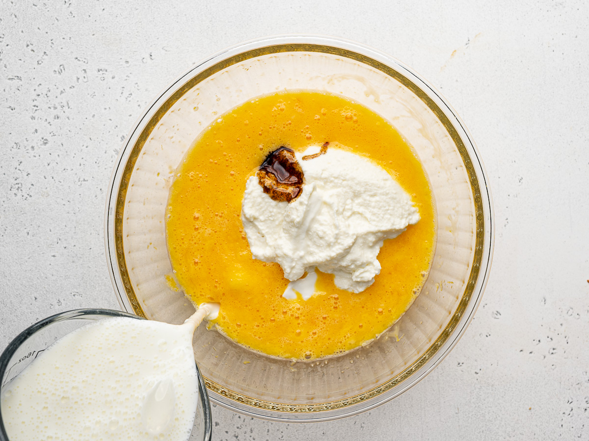Adding ricotta and buttermilk to egg mixture in glass mixing bowl.