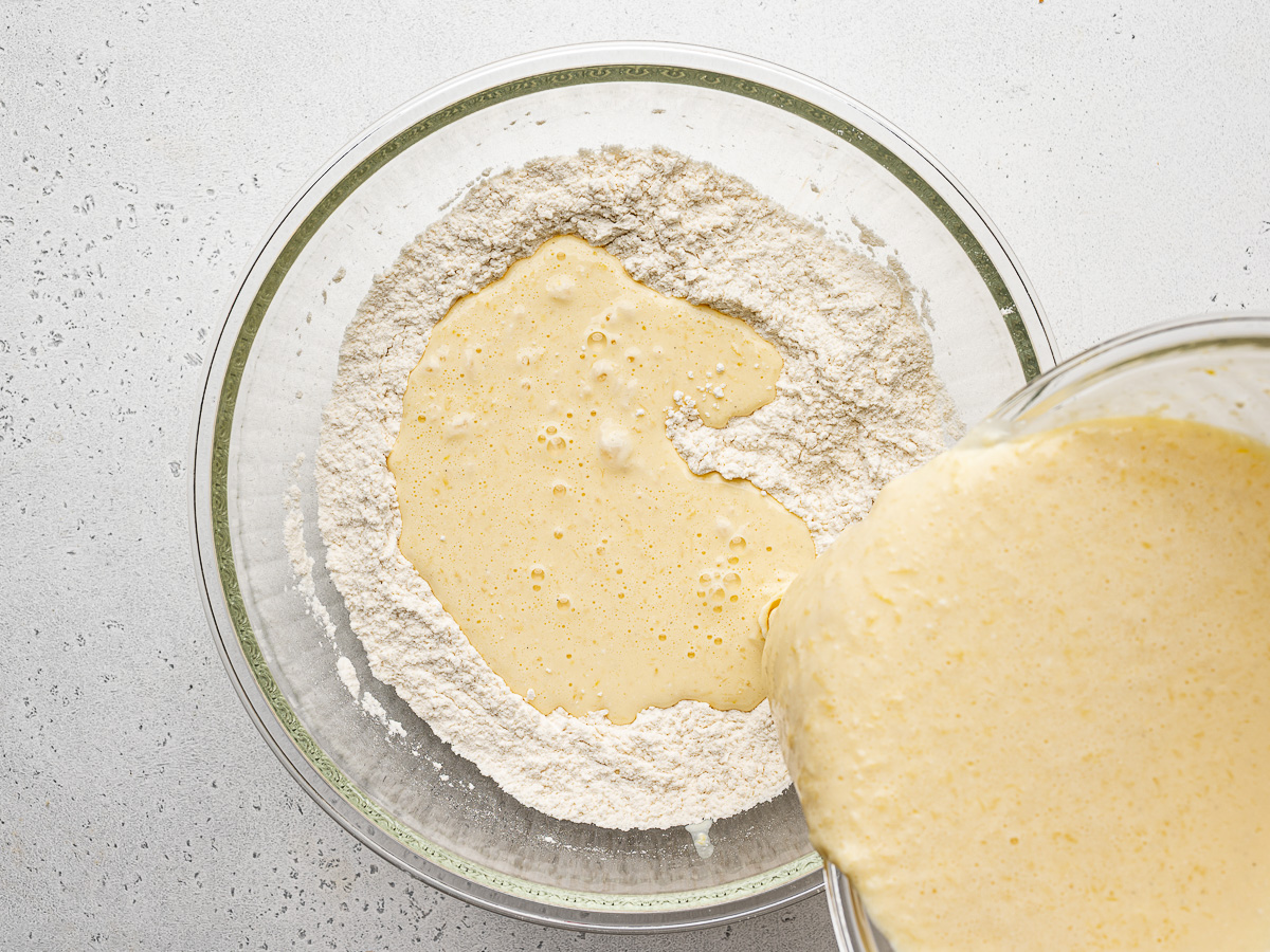 Pouring wet ingredients over dry ingredients in glass bowl.
