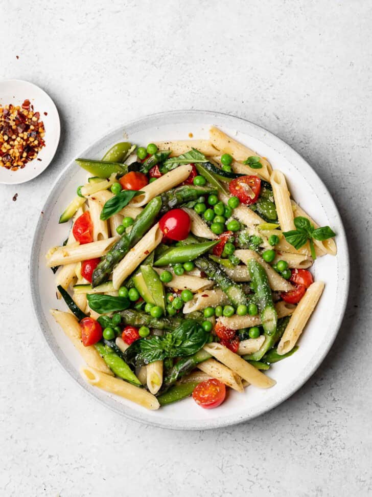 pasta primavera served on plate with red pepper flakes on the side