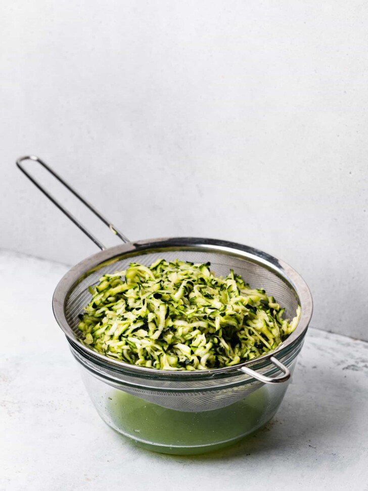 grated zucchini draining in colander over bowl 