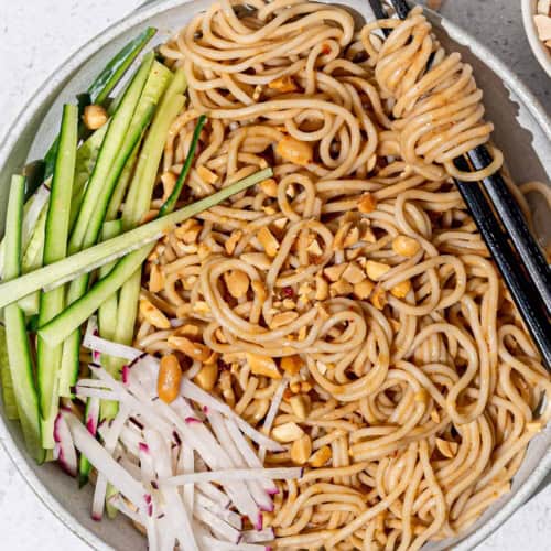 Takeout-style sesame noodles served in bowl with cucumbers and radishes